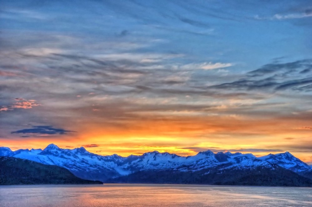 a group of clouds in the sky over a snow covered mountain